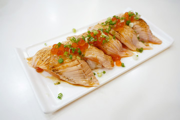 Closeup of salmon sushi on a white plate with salmon roe and chopped spring onion, Aburi style refers to nigiri sushi, the fish is partially grilled topside and partially raw - Japanese food style.