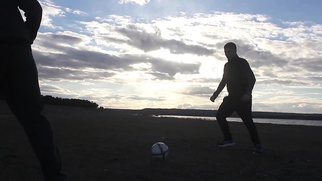 Beautiful sunset and silhouettes of men playing football, kick a soccer ball, goalkeeper catches ball. Silhouette of soccer player ready to execute penalty kick on the field.