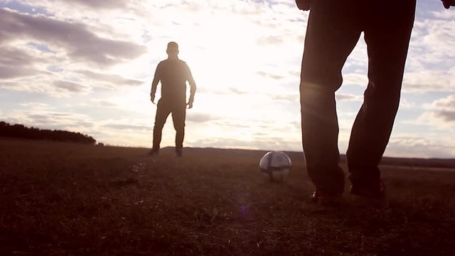 Beautiful sunset and silhouettes of men playing football, kick a soccer ball, goalkeeper catches ball. Silhouette of soccer player ready to execute penalty kick on the field.