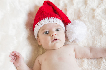 Portrait of  a cute baby girl awake, looking at the camera. She is wearing a santa Christmas hat. White blanket background