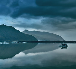 Glacial lagoon in Iceland in the fall. Cloudy foggy weather, mountains on the horizon. The glacial lake reflects the sky, glacier and mountains