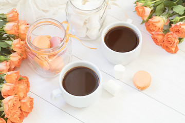 Orange mango macaroons, cup of coffee, marshmallow and fresh little roses on light wooden background. Sunlight. Coloring and processing photo with light vintage style. Shallow depth of field.