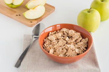 Cornflakes in bowl, fresh apples both whole and cut in pieces on wooden board, on white background. Healthy breakfast concept