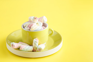 cup full of sweet twisted  marshmallow on bright yellow background