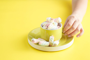 hand holding bowl of sweet Marshmallow pastel isolated on yellow background.