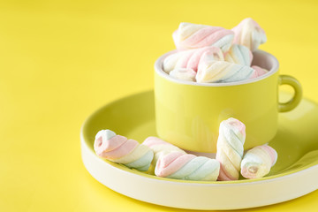cup full of sweet twisted  marshmallow on bright yellow background