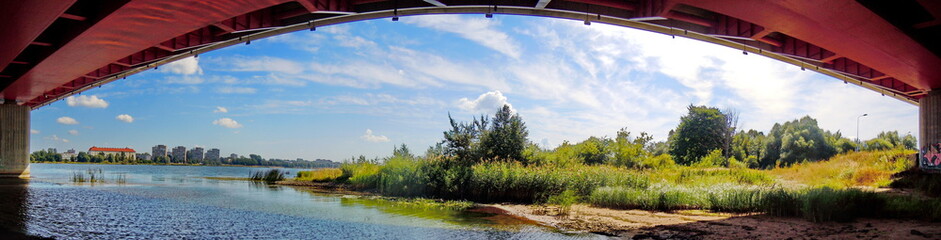 Obraz premium Panoramic view of grassy riverside, bridge and distant town