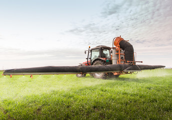 Tractor spraying pesticide on wheat field with sprayer