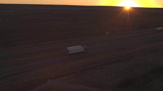 AERIAL: Flying above cars and trucks driving on busy highway through the desert at dusk. Freight semi trucks transporting goods, personal cars on a road trip, people traveling on early summer evening