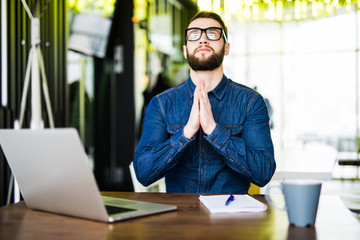 Praying for success. Front view of thoughtful young man holding hands on chin and looking up while sitting at his working place in office