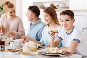 Pleasant smiling boy having breakfast with his family