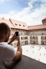 Fototapeta na wymiar Male traveler on the background of Arcades in Wawel Castle in Cracow. Poland. Renaissance. A man takes photos on his mobile phone from the second floor of the courtyard in Wawel Castle