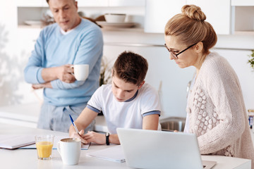 Obraz na płótnie Canvas Diligent boy doing homework with his parents