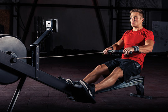 Young Man Using Rowing Machine In The Gym