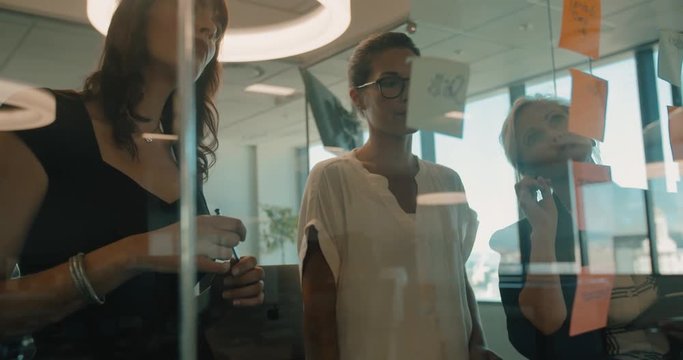 Female executives discussing over sticky notes on glass wall