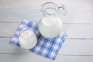 A jug of milk and glass of milk on a wooden table