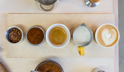 Overhead shot of coffee, beans, milk and latte on wooden table in coffee shop