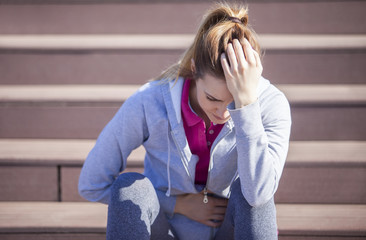 Young woman with abdominal pain after sitting on the steps of recreational running