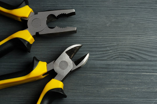 Side cutters and combination pliers on a dark wooden background.
