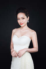 Fashion portrait of beautiful young asian woman in white dress over dark background.