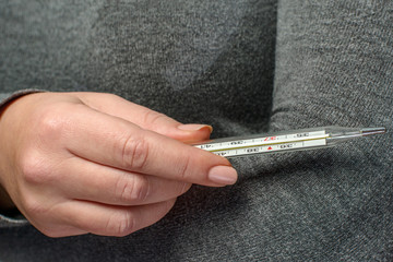 Holds the thermometer. Close-up of thermometer in woman's hand. Measurement of body temperature with a thermometer.