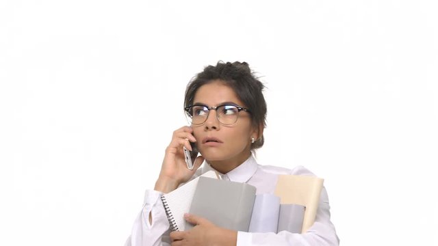 Happy smiling student girl talking on mobile phone while holding stack of books isolated 