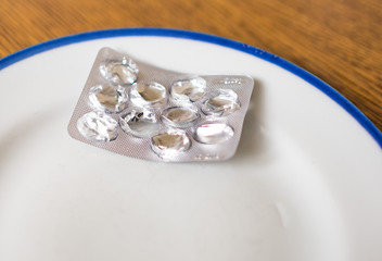 Set of pills in a plastic and foil package lying on white tray with blue rim