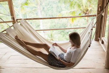 Young woman relaxing in hammock and reading book.