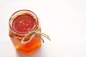 Honey in a glass jar on a wooden white board.