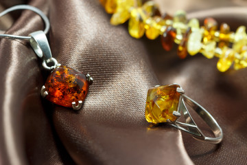 closeup jewelry with  authentic  natural baltic amber : silver ring and pendant, on brown atlas surface. Bracelet on background. small DOF.