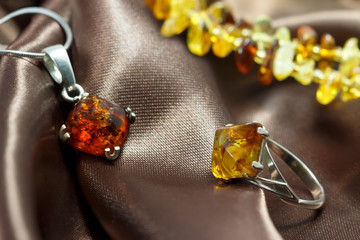 closeup jewelry with  authentic  natural baltic amber : silver ring and pendant, on brown atlas...