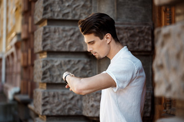 Young successful businessman looking at watch, walking around sunny city.