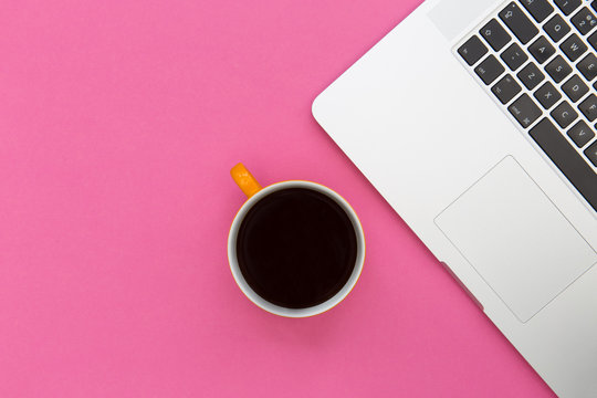 Coffee cup and laptop computer overhead on bright pink background