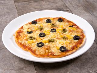 Cheesy Pizza topped with corn and olives served in a white plate on wooden background