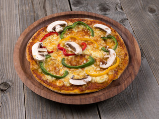 Cheesy mushroom capsicum pizza served in a wooden plate on wooden background