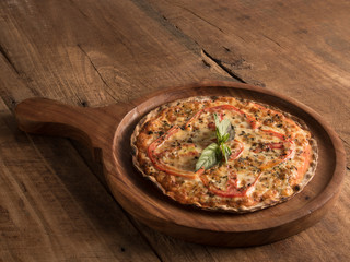 margarita pizza served in a wooden pizza paddle on wooden background
