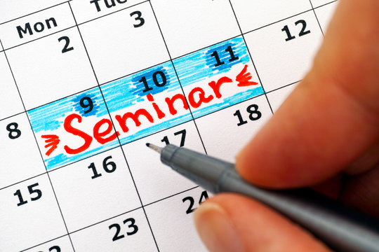 Woman fingers with pen writing reminder Seminar in calendar
