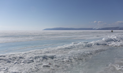 Transparent blue ice hummocks on lake Baikal shore. Siberia winter landscape view. Snow-covered ice of the lake. Big cracks in the ice floe.
