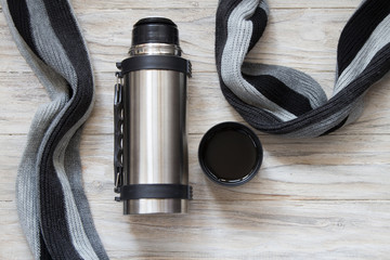 Open thermos flask and scarf on a woden background. Top view