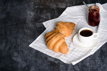 Picture of croissants, pot with jam and coffee cup aside on grey table