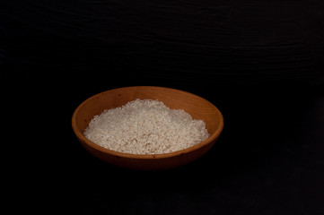 rice in wooden bowl with wooden spoon on black background empty space