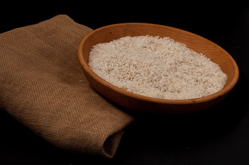 Closeup rice in wooden bowl with wooden spoon on black background empty space