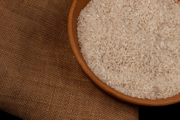 Closeup rice in wooden bowl with wooden spoon on black background empty space