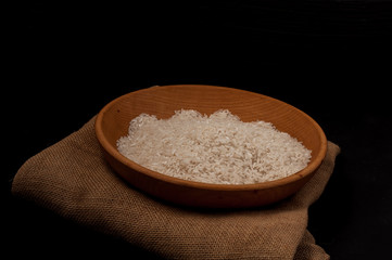 Closeup rice in wooden bowl with wooden spoon on black background empty space