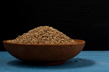 Wooden bowl with pearl barley on blue and black background. Close-up.