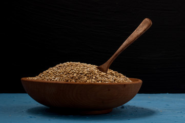 Wooden bowl with pearl barley on blue and black background. Close-up.