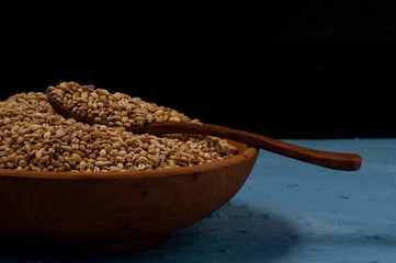 Wooden bowl with pearl barley on blue and black background. Close-up.