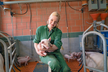 Junge Landwirtin im Schweinstall stolz mit Ferkel auf dem Arm