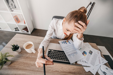 young stressed businesswoman with laptop and documents sitting at table in office