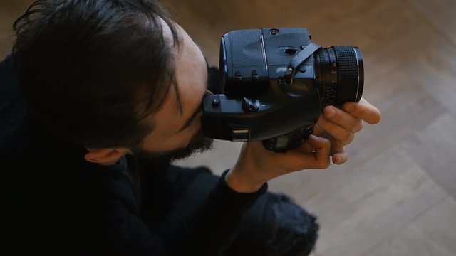 Photographer composing and framing image, focusing and shooting with medium format film camera in studio, professional male artist working with portrait angle lens